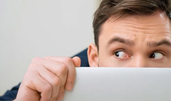 Foto van een man die zich verschuilt achter een laptop